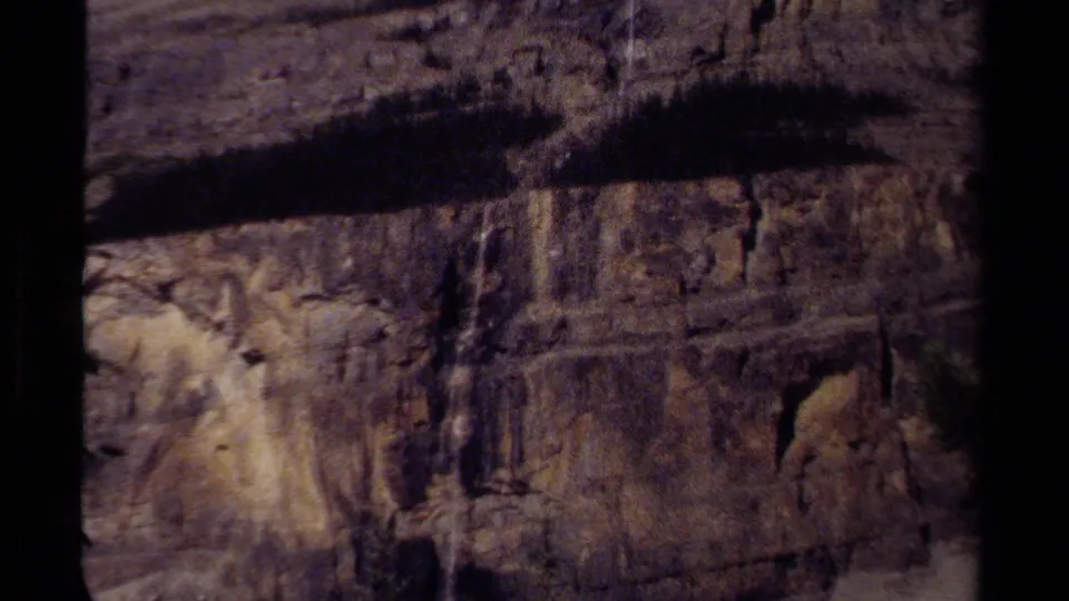 Close 8mm view of a British Columbia rocky cliff face, with layered stone texture and a shadowed ridge across the upper frame.