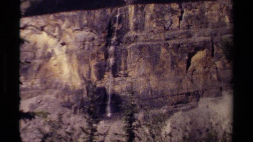 1979 British Columbia 8mm view of a rocky cliff face, with a slim waterfall visible against the darker stone.