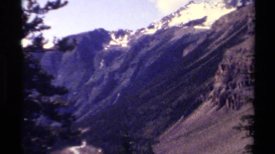 1979 British Columbia 8mm mountain view with snow patches along the ridgeline and dark trees framing the foreground.