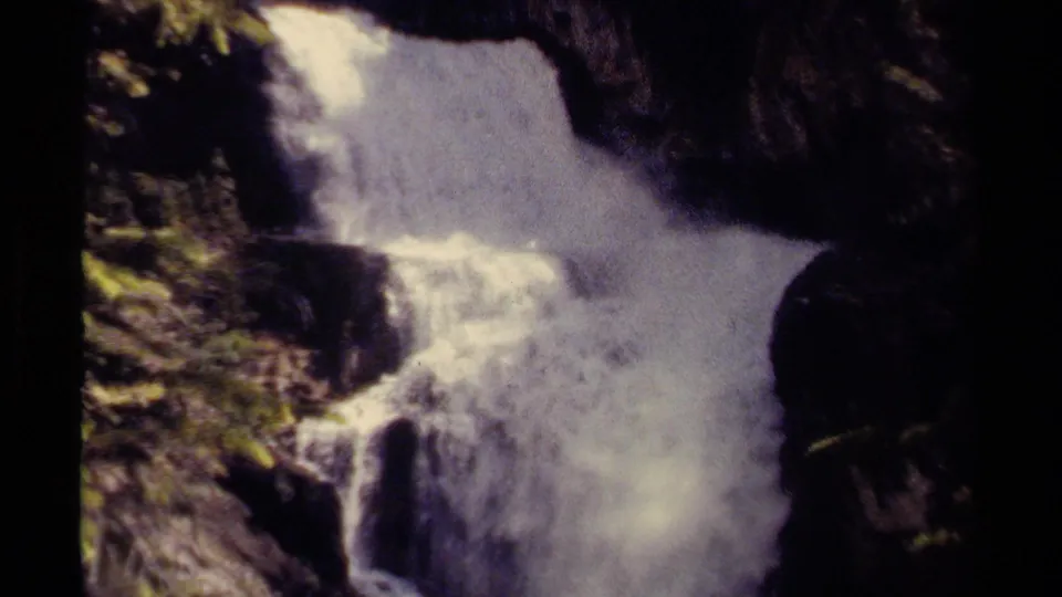 Rushing waterfall in British Columbia, Canada, filmed on 8mm with dark rock faces and patches of green foliage around the water.