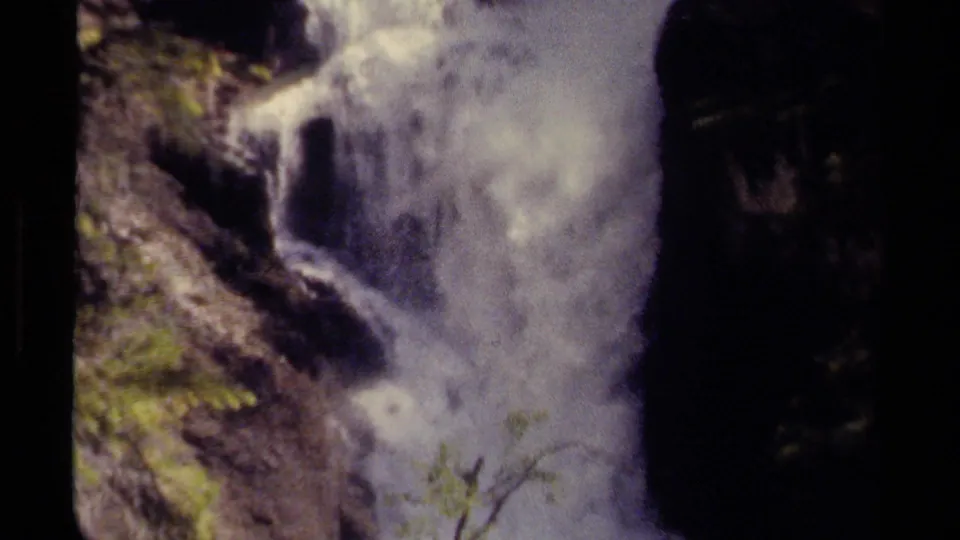Close 8mm view of a powerful waterfall cascading down a rocky British Columbia mountainside, with soft grain and faded color.