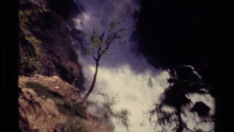 Wider 1979 home-movie view of a British Columbia waterfall course with a small tree, rocky banks, white water, and deep shadow.