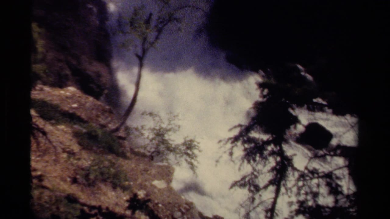 1979 British Columbia 8mm frame showing a waterfall cascading through rocks with mist, trees, and shadowed canyon edges.