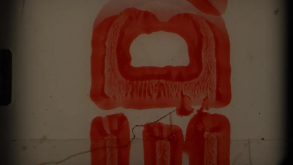 A red graphic or object fills the frame on pale backing in 8mm footage, with dark gate edges and visible film wear.