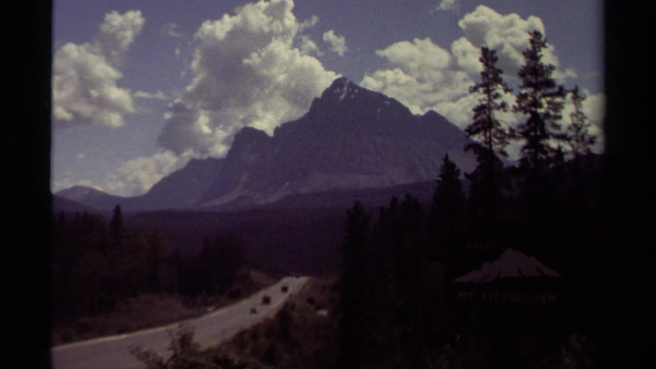 1979 British Columbia 8mm view of a winding forest road leading toward a mountain under scattered clouds.