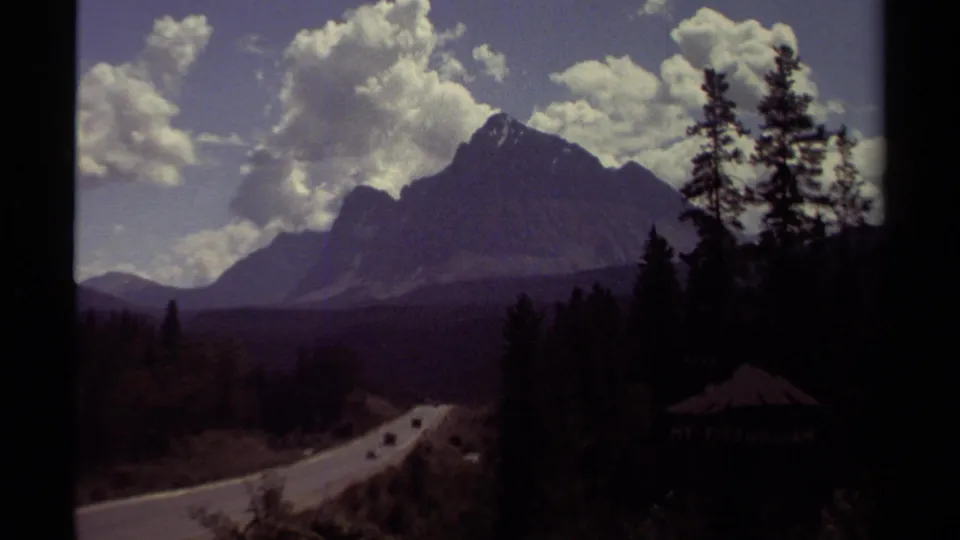 1979 British Columbia 8mm view of a winding forest road leading toward a mountain under scattered clouds.