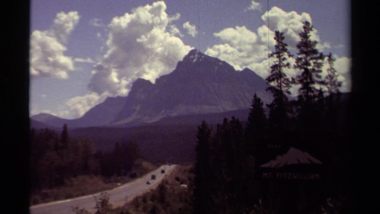 1979 British Columbia roadside view with a mountain backdrop, evergreen trees, passing cars, and a partly visible Mt. Fitzwilliam sign.