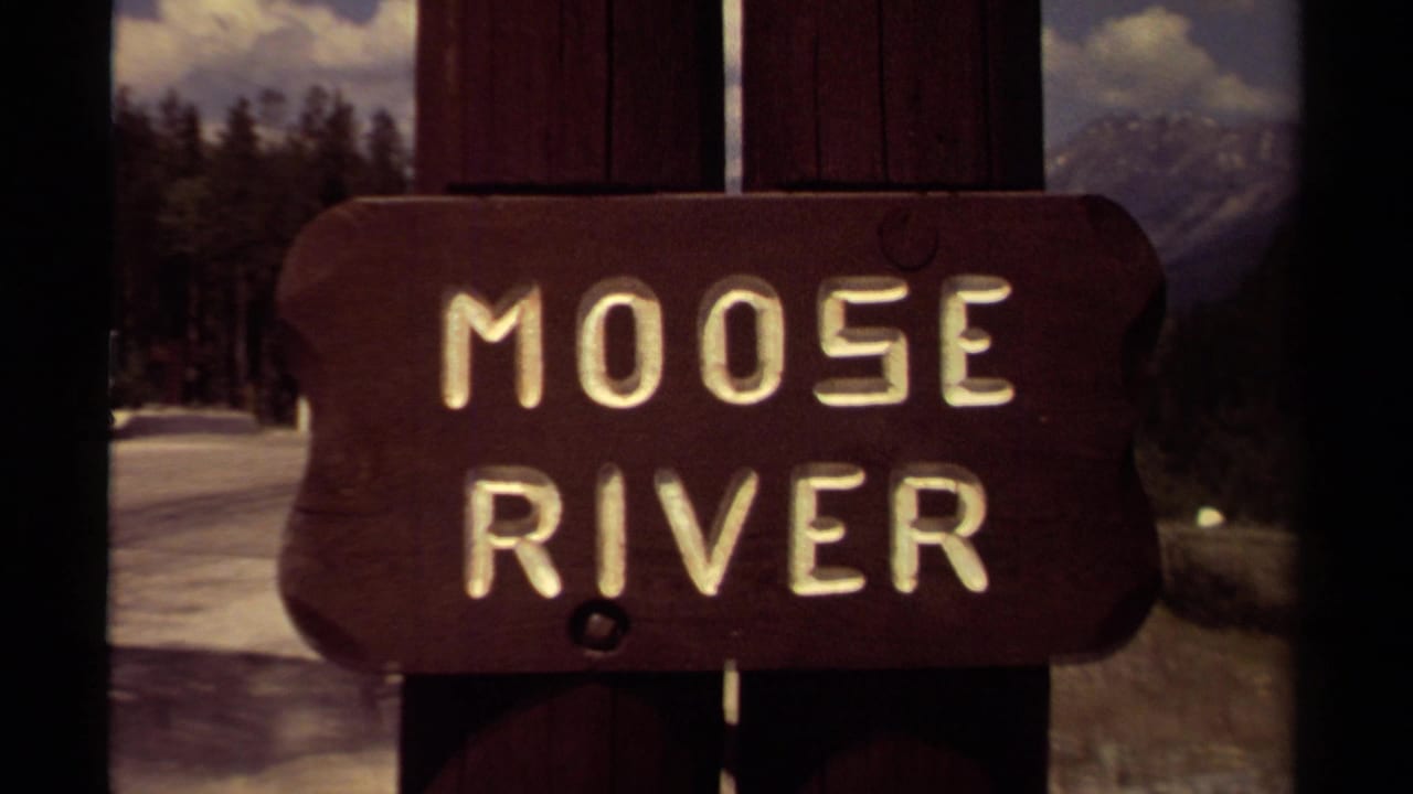 1979 British Columbia 8mm frame showing a carved Moose River sign in front of snowy forest and distant mountains.