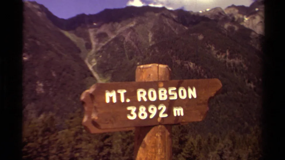 A visitor-shot 8mm frame shows the Mt. Robson 3892 m wooden sign with British Columbia mountain ridges in the background.