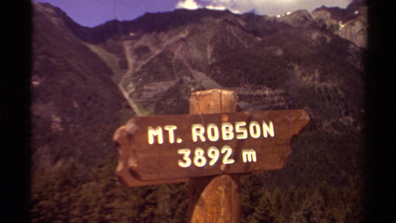 1979 8mm frame of a wooden Mt. Robson 3892 m sign in British Columbia, with rugged forested mountains in the background.