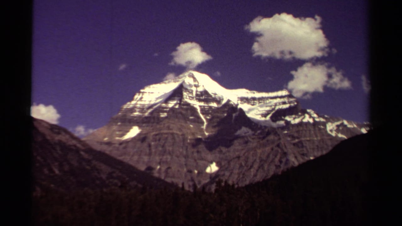 1979 8mm view of a snowy mountain peak in British Columbia with rocky ridges, clouds, and a dark foreground slope.
