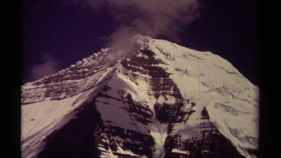 1979 8mm close view of a snow-covered alpine slope in British Columbia, with layered rock, cloud cover, and soft film grain.