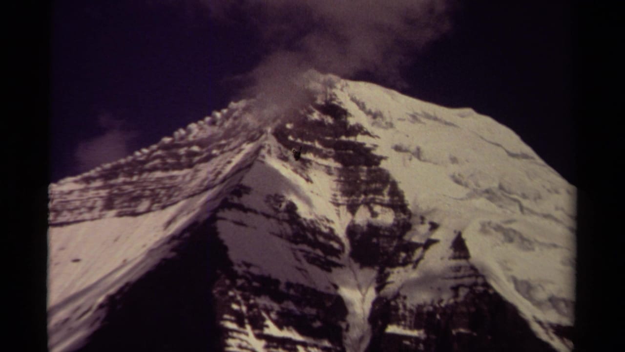1979 8mm frame from British Columbia showing a snowy mountain peak, dark sky, and drifting cloud or mist near the summit.