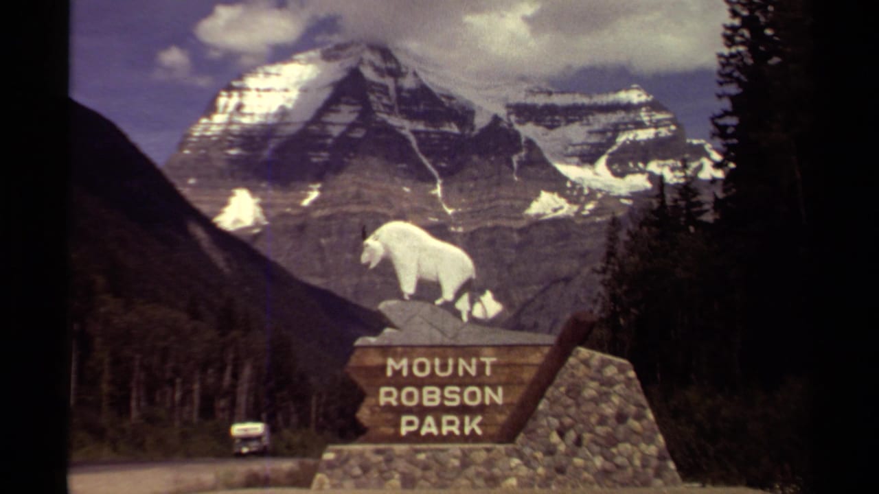 1979 British Columbia 8mm frame showing the Mount Robson Park sign, a small car on the road, forest, and snow-capped mountain peaks.