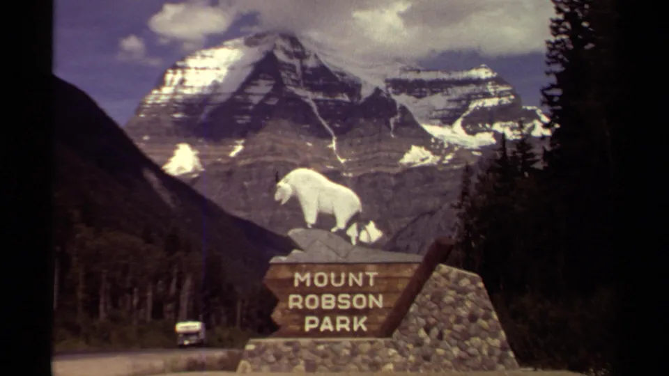 1979 British Columbia 8mm frame showing the Mount Robson Park sign, a small car on the road, forest, and snow-capped mountain peaks.