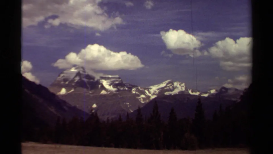 1979 British Columbia 8mm frame of Mount Robson area mountains, forested slopes, and scattered clouds in a wide scenic view.