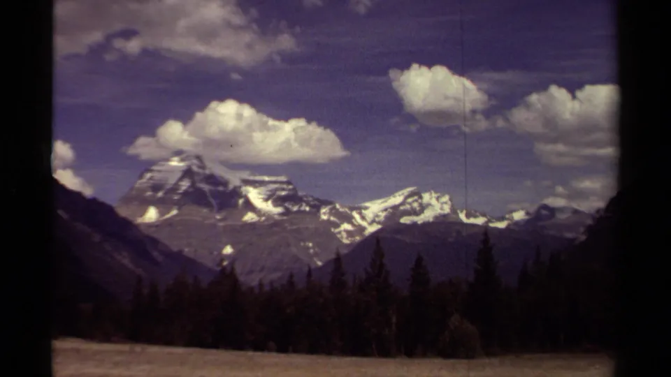 1979 British Columbia 8mm frame showing a distant Mount Robson area peak, snowy ridges, forest, and cloud formations.