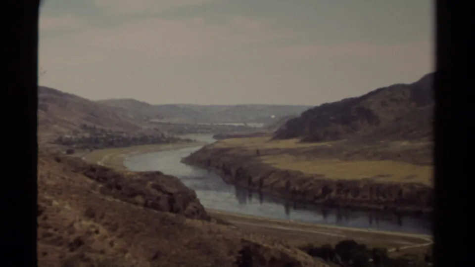 British Columbia 1979 home-movie panorama showing a winding river, arid slopes, fields, and a small distant settlement.
