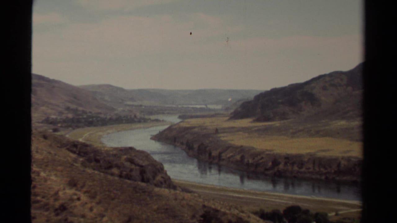1979 British Columbia 8mm frame showing a river bend between dry rolling hills under a pale sky.