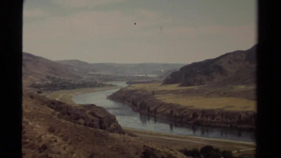 1979 British Columbia 8mm frame showing a river bend between dry rolling hills under a pale sky.