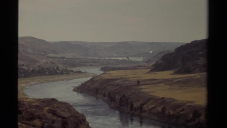Vintage 8mm British Columbia frame showing a river curve, dry fields, and distant valley land during a slow scenic zoom.