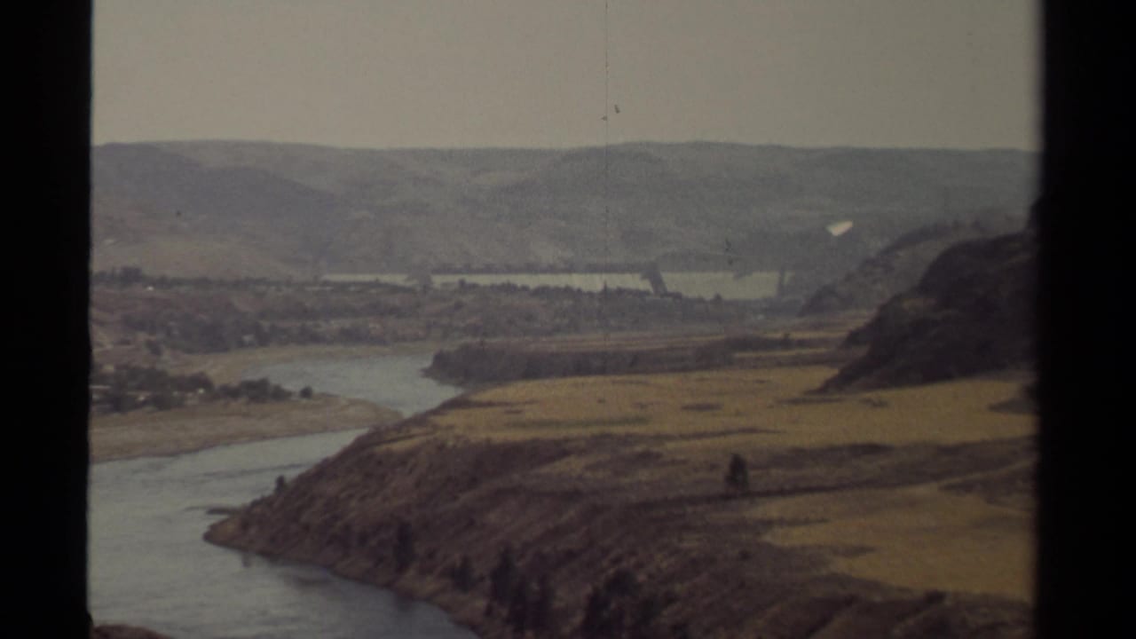 1979 British Columbia 8mm view of a winding river valley with dry slopes, distant hills, and dam structures partly visible below.