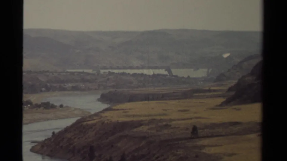 Supported by metadata as British Columbia in 1979, the frame shows a river bend, dry terrain, distant hills, and partial dam infrastructure.