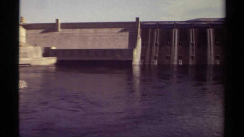 1979 British Columbia 8mm frame with dam spillway gates, concrete wall, calm water reflections, and heavy black frame edges.
