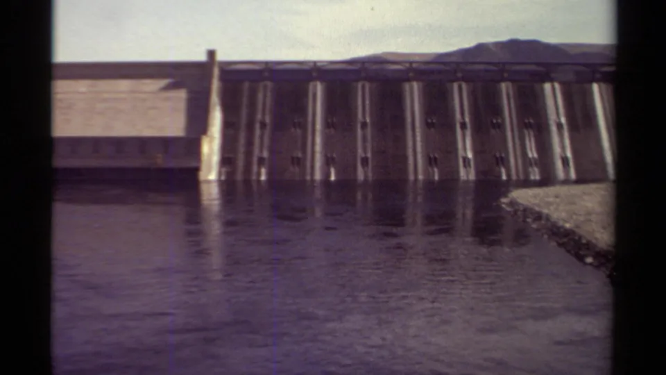 1979 British Columbia 8mm frame showing a closer view of dam gates, foreground water, distant hills, and dark film borders.