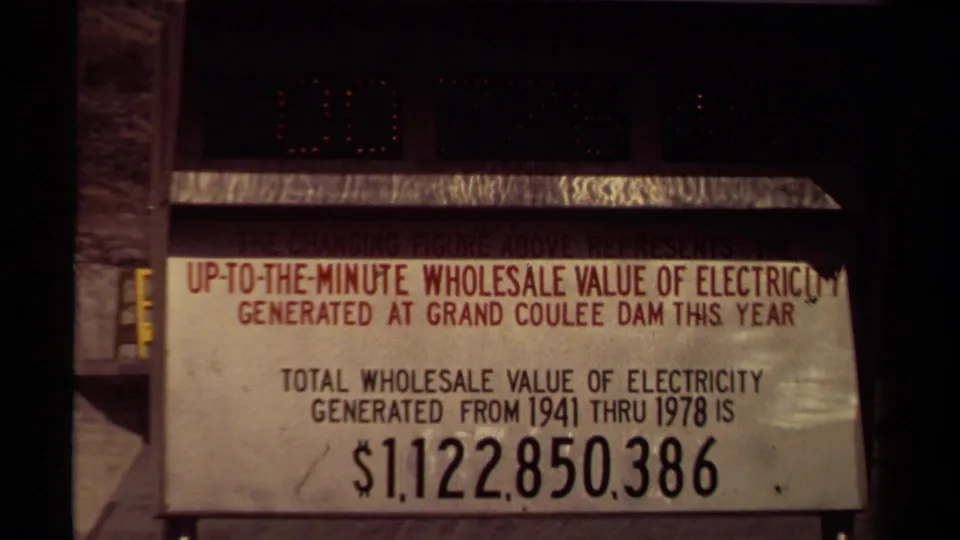 Final 1970s 8mm frame of the Grand Coulee Dam electricity value sign, showing the printed total and dim changing-number display.