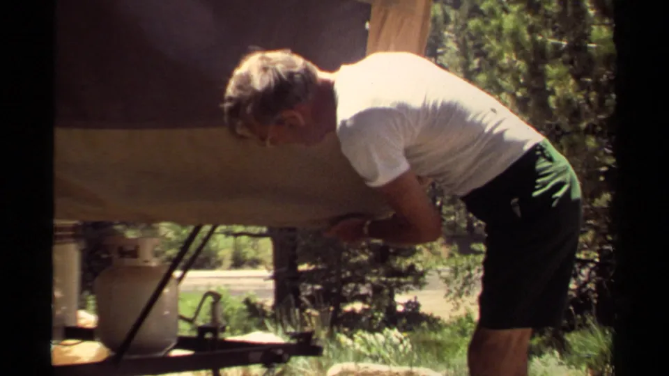Mendocino campsite frame showing a man leaning under the pop-up camper edge, apparently adjusting a support or awning area.