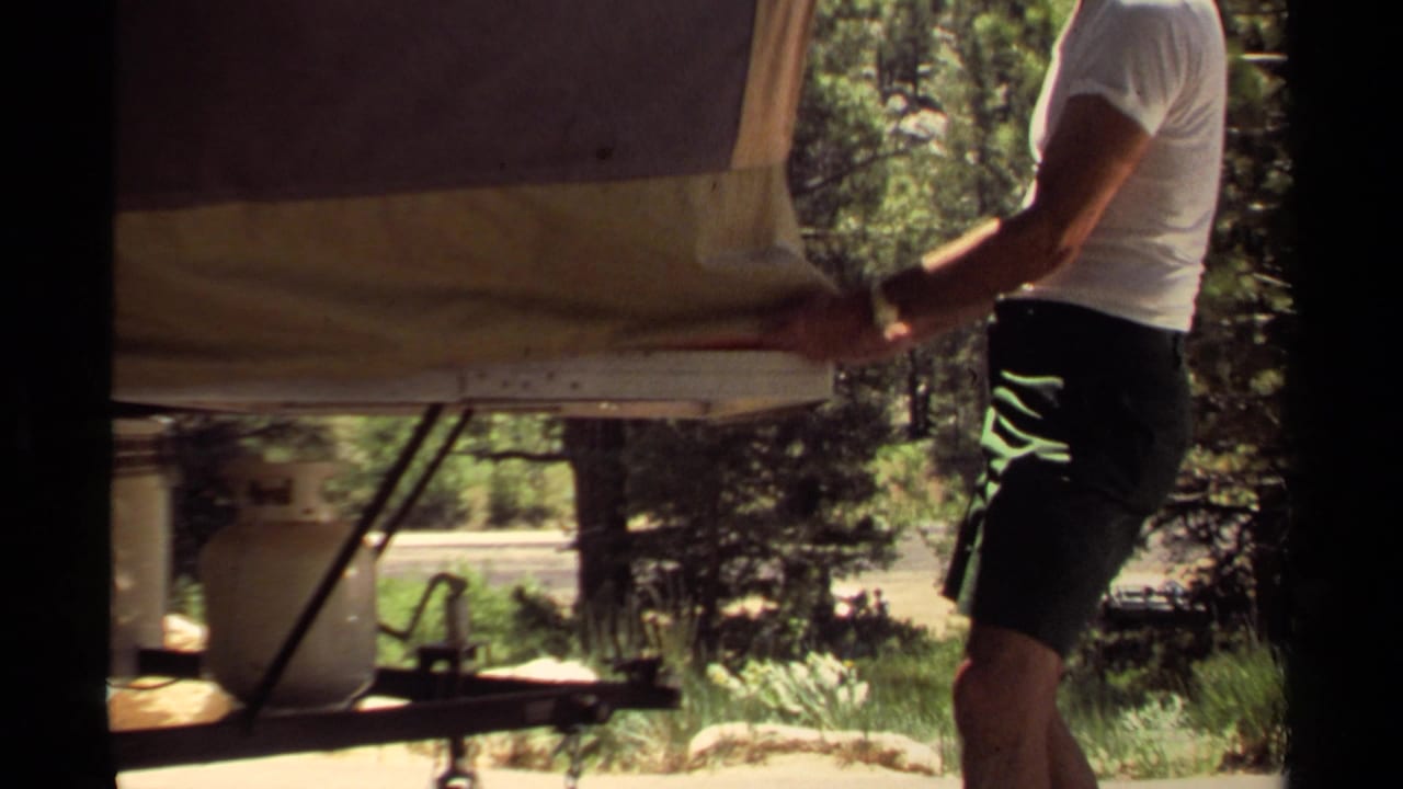 Man stands beside a small trailer, holding or straightening its canvas cover.