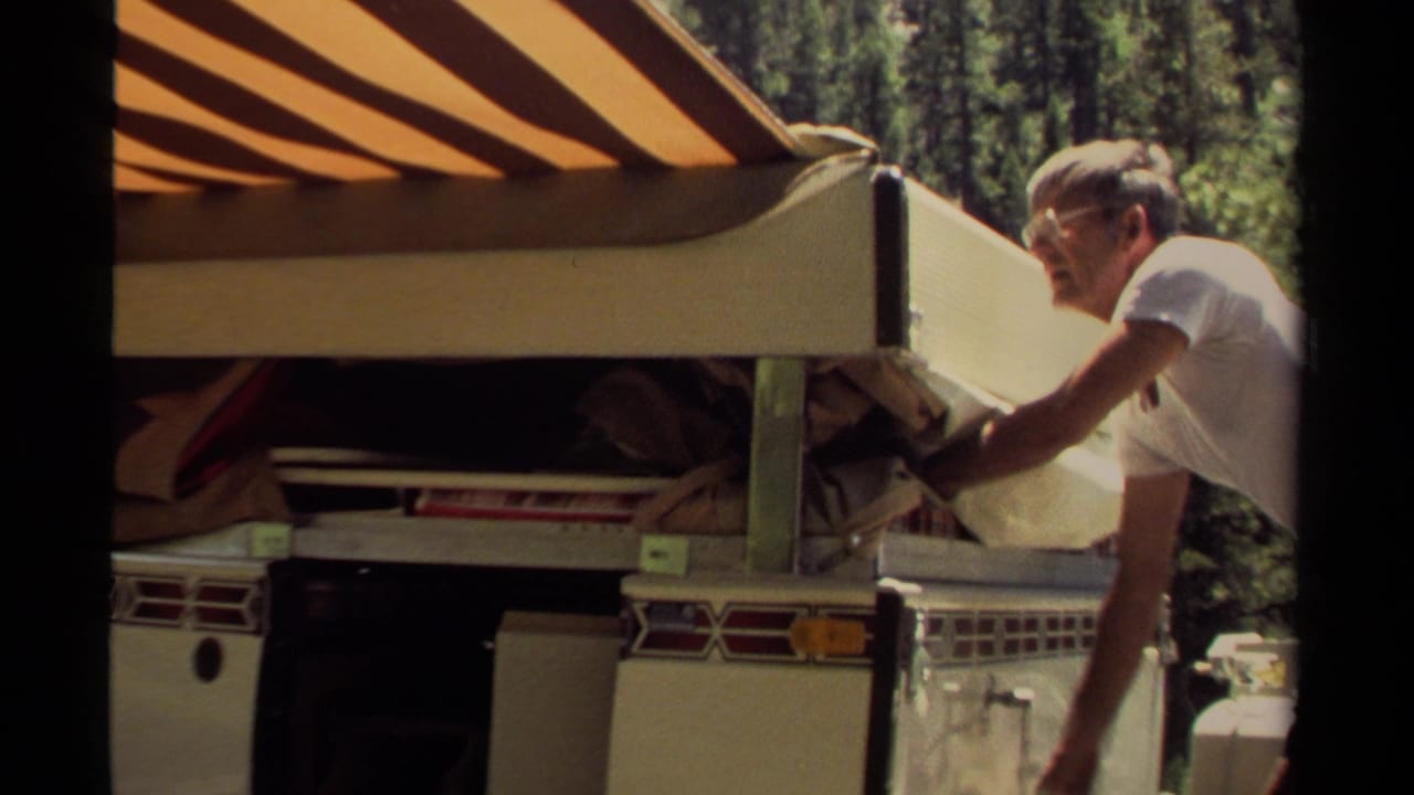 Man stands beside the rear of a camper trailer with its canvas side open and awning overhead.