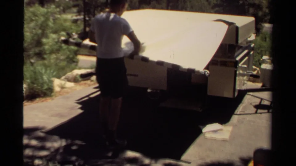 In Mendocino, California, a man in a white T-shirt stands at the rear of a tan pop-up camper in 1980 home-movie footage.