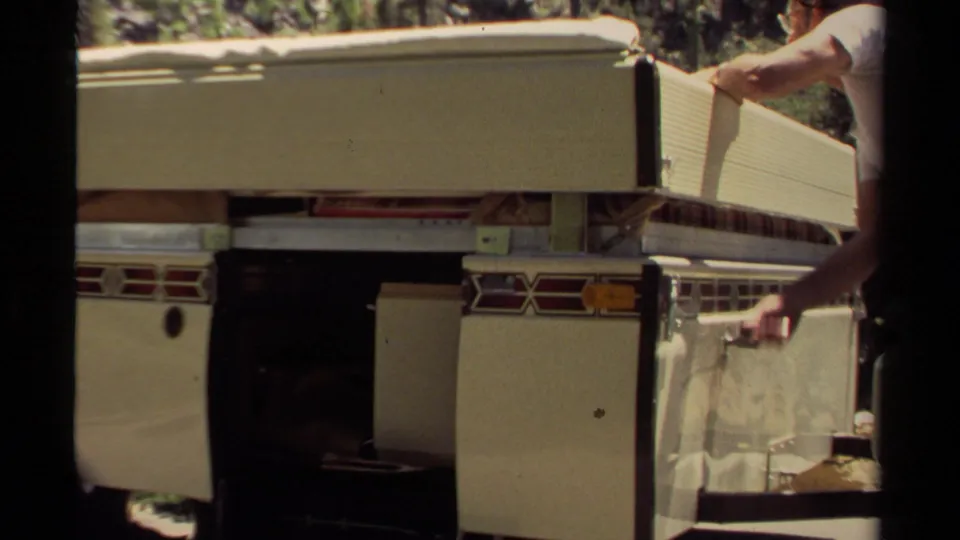 Close 8mm view of the camper side as the man pulls or guides the canvas and panel down during packing.