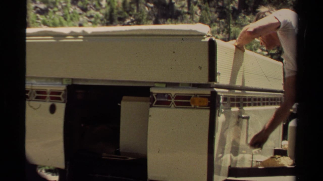 White vintage camper trailer in Mendocino, 1980, with a partially visible adult operating the side compartment mechanism.
