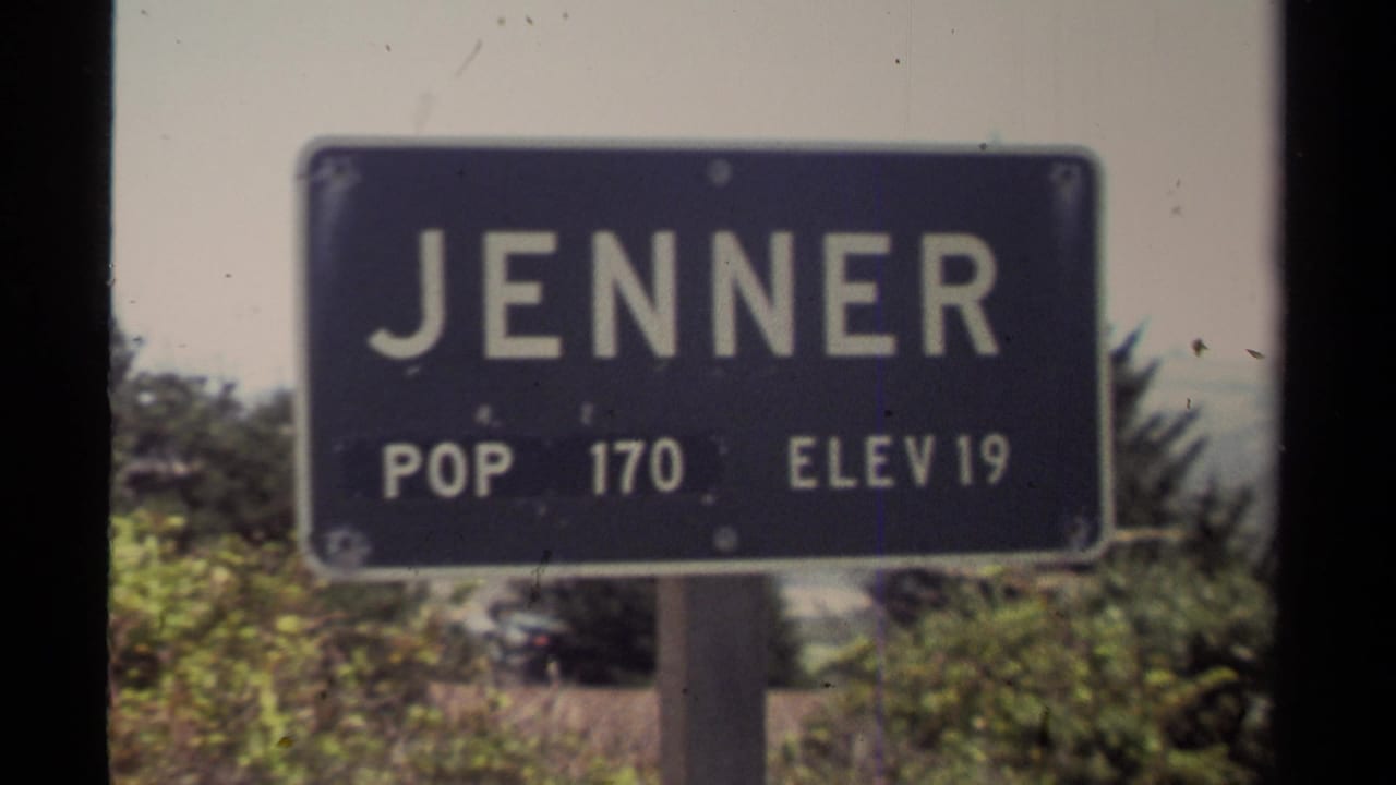 Sunlit 1980 8mm frame of the Jenner town sign in California, with POP 170 and ELEV 19 visible against roadside greenery.
