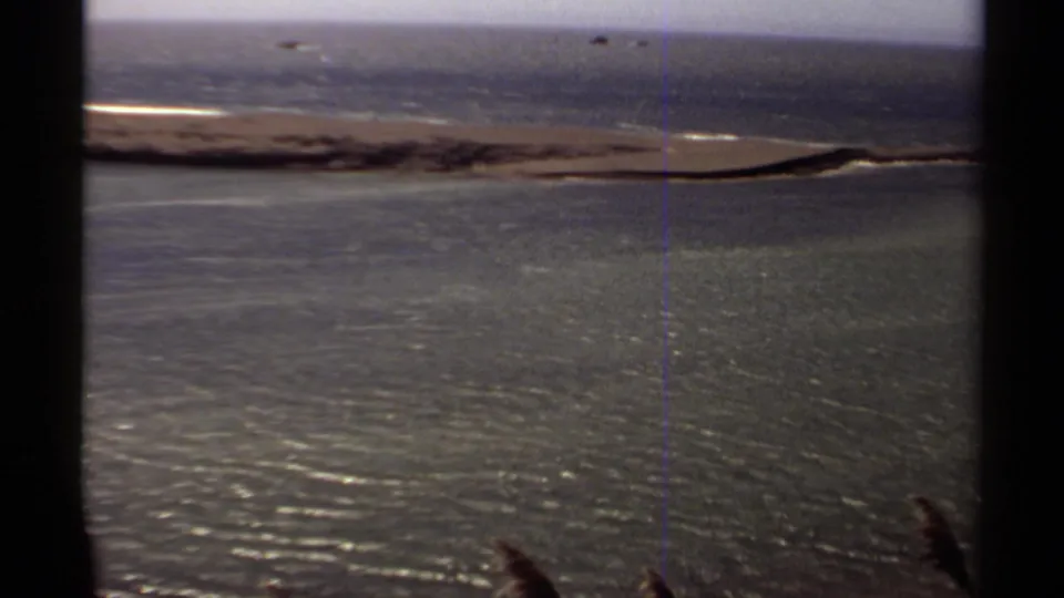 1980 Mendocino coastal view with rippled water, a narrow sandbar, low surf, and dark foreground silhouettes from the filming position.