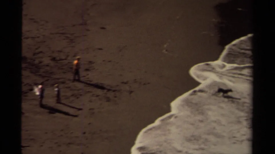 Close 1980 8mm beach view in the Mendocino coastal cove, with foamy waves reaching wet sand and dark textures across the shoreline.