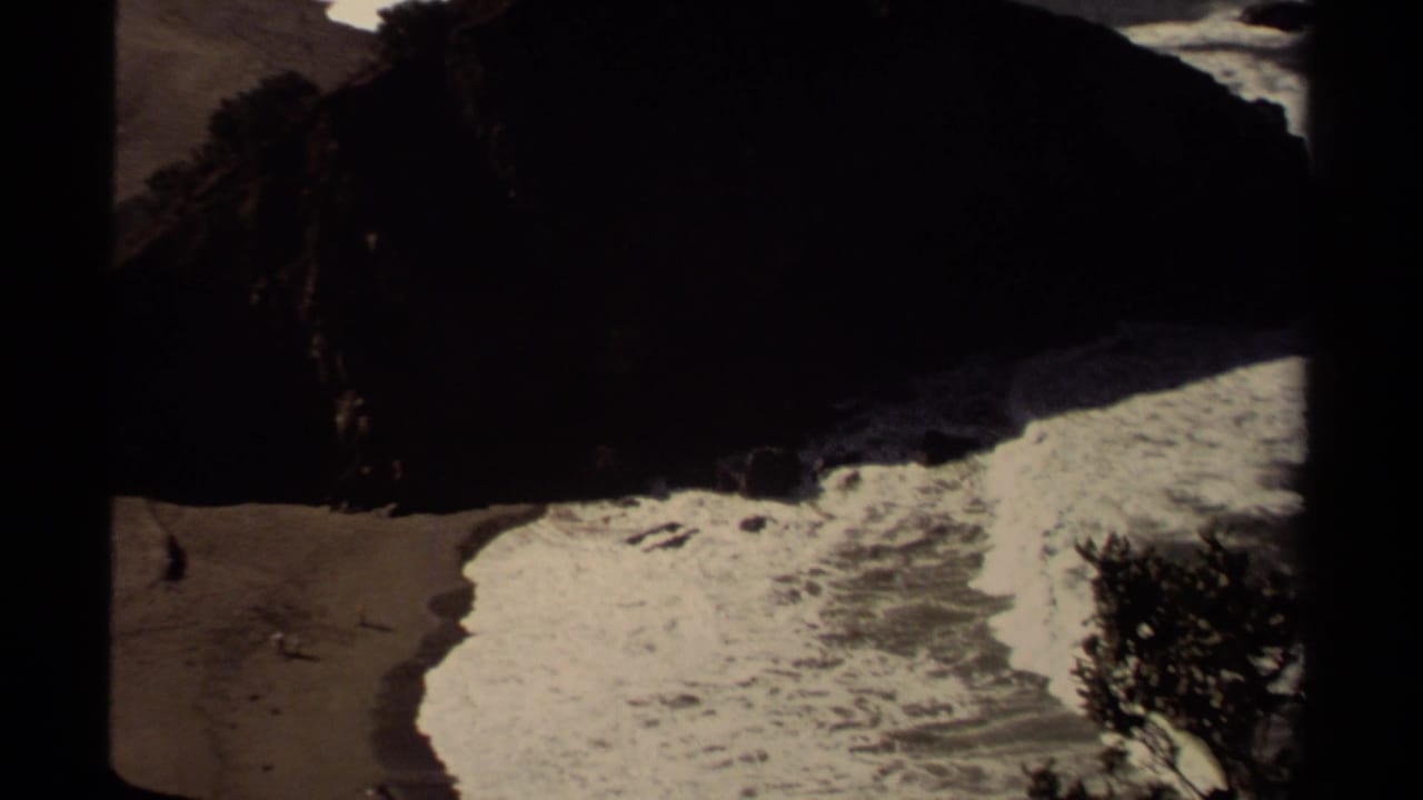 Waves curl across a beach beside a large dark rock outcrop.