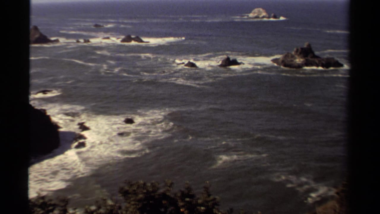1980 8mm view of the Mendocino coast with Pacific surf, offshore rocks, sea stacks, and dark frame edges.