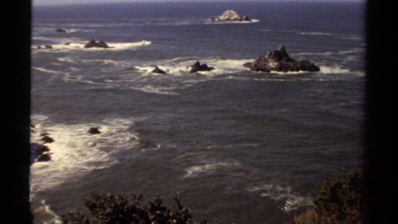 Wide ocean view with foamy surf surrounding jagged coastal rocks.