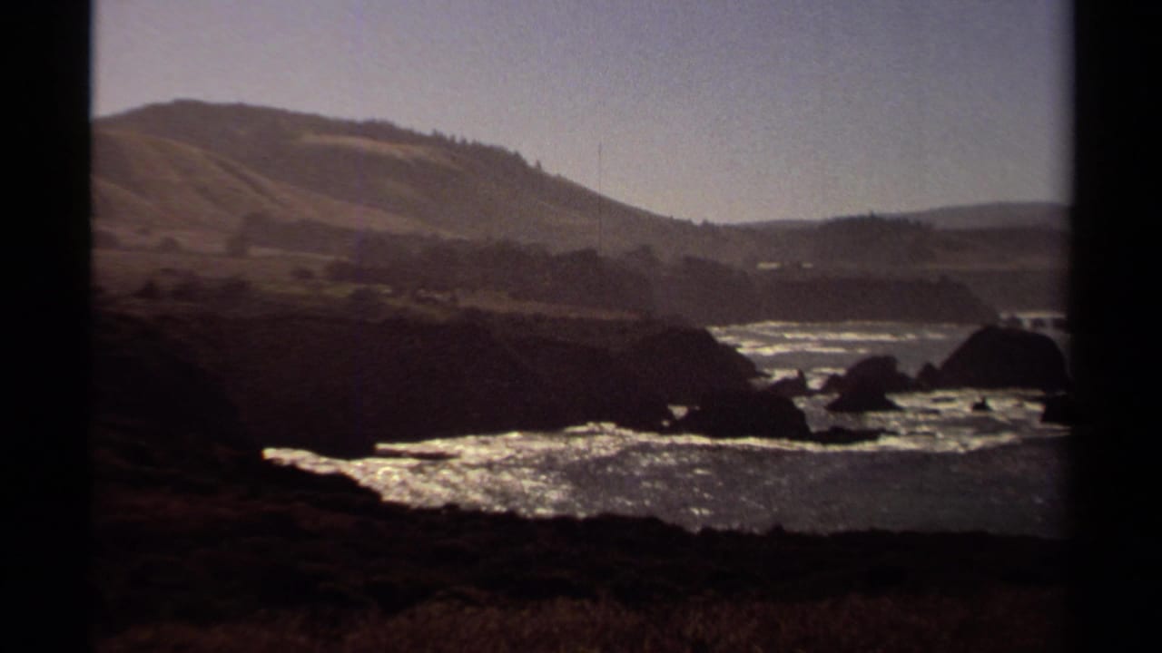 Rocky shoreline and bright ocean water with hills in the background.