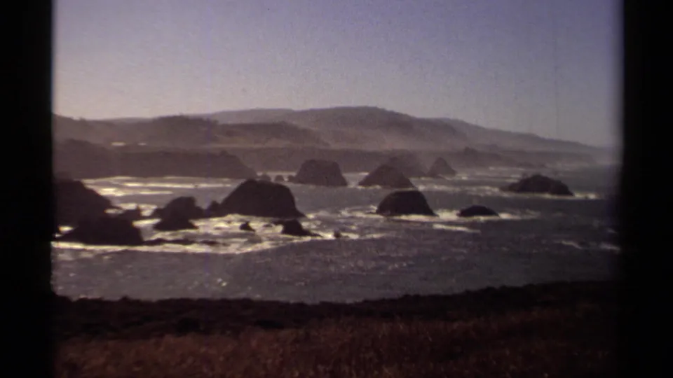 Mendocino, California coastal rocks and churning water appear in a warm, grainy 1980 8mm travel view from above the shore.