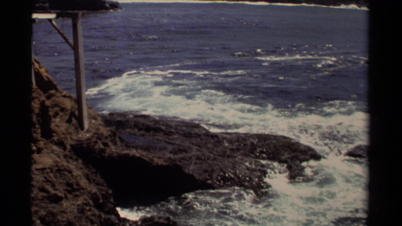 Waves break against dark rocky shoreline beside a simple wooden post structure.