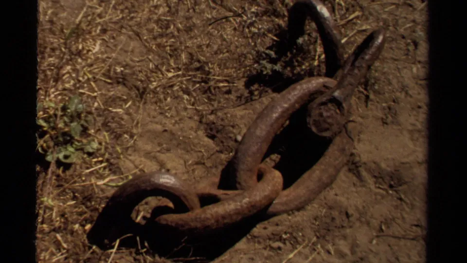 Close-up 1980 home-movie frame of a rusted chain on dry ground near the Mendocino coast.