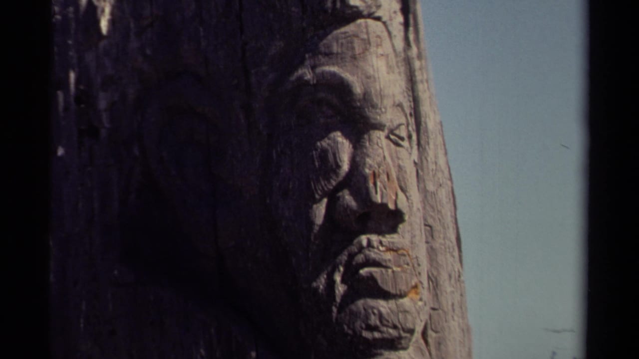 1980 8mm Mendocino-area frame showing a weathered carved wooden face in close-up with pale sky and dark film-edge borders.