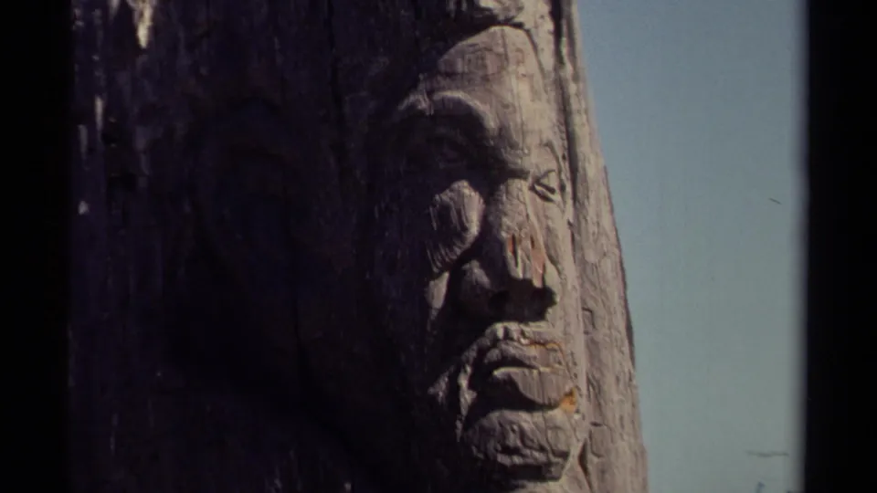1980 8mm Mendocino-area frame showing a weathered carved wooden face in close-up with pale sky and dark film-edge borders.