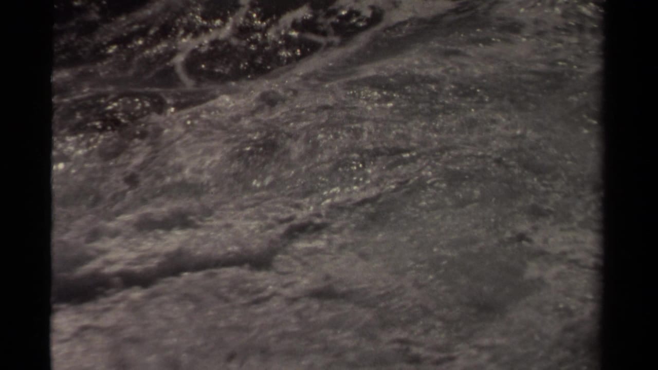 Black-and-white 8mm frame from Mendocino metadata showing rough ocean water with foam and dark shapes partly obscured by surf.
