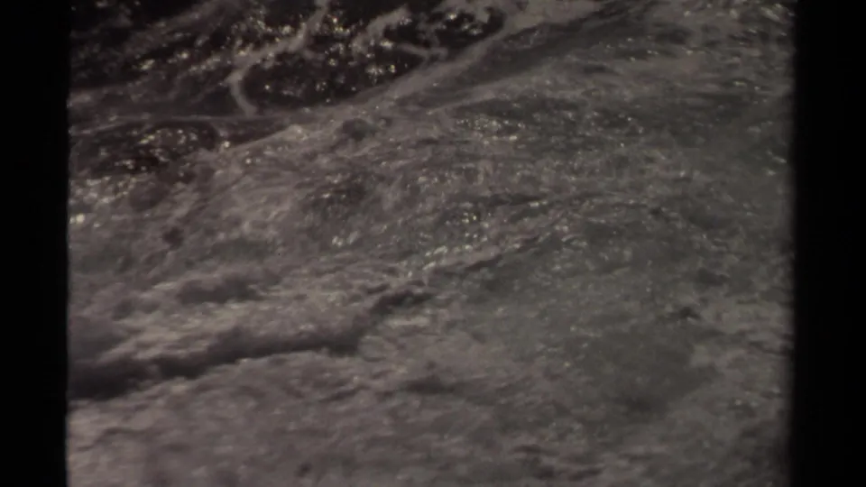 Black-and-white 8mm frame from Mendocino metadata showing rough ocean water with foam and dark shapes partly obscured by surf.
